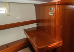 Wood-paneled boat cabin with a fold-down desk and built-in storage, small window with a curtain to the left.