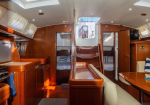Interior of a luxury sailboat cabin with polished wood cabinetry, a kitchenette, central bar, and dining seating.