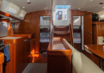 Luxurious yacht cabin interior with a wooden galley on the left, beige seating and table on the right, and sleeping berths visible at the rear.