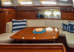 Interior of a sailboat salon with cream seating, navy striped cushions, and a wooden dining table with a small ship wheel centerpiece.