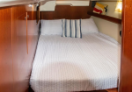 Wood-paneled yacht cabin with a neatly made bed, white quilt and two pillows.