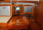 Wood-paneled navigation station aboard a boat with a curved chart table, radio, GPS display, and control panel of switches on the wall left of center.