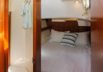Cozy boat cabin with a neatly made bed, white striped bedding, and three pillows (one striped) against a wooden headboard, towels hanging nearby.