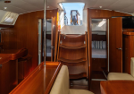 Wood-paneled yacht cabin with a central curved stairway and beige seating, leading to forward berths