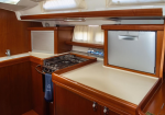 Compact yacht galley with cream countertops, polished wood cabinetry, stove, and a small fridge nearby.