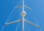 White radio antenna mast with supporting crossbars and multiple guy wires against a clear blue sky, including a circular antenna at mid-height.