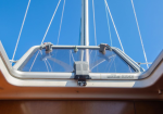 Looking up at a sailboat's transparent cabin hatch with rigging lines against a clear blue sky, viewed from inside the cabin toward the deck above.