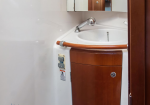 White oval sink with chrome faucet set in a wooden curved cabinet, on a small boat bathroom exterior edge visible by a cabin door edge.