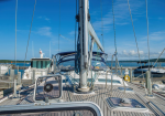 Sailboat docked at a marina with a tall mast, rigging, and other boats along the pier under a blue sky.