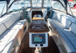 Sailboat cockpit with cushioned benches, a wooden center table, and navigation screen mounted at leg level under the table edge