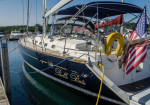 A sleek sailboat named 'Belle Bete' docked at a marina, with a yellow life ring and an American flag on the stern.