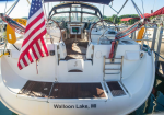 Back view of a white sailboat docked at a marina, with an American flag and wooden swim platform; 'Walloon Lake, MI' on the stern