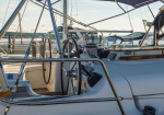 Sailboat cockpit with two wooden steering wheels and stainless rails, moored at a sunny marina.