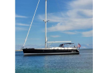 Side view of a sleek black-and-white sailboat anchored on calm blue water under a clear sky, with an American flag at the stern.