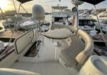 Yacht cockpit at sunset with curved cream seating around a round table on a white deck in a marina.