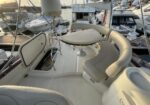 Cream curved bench seating around a round table on a white yacht deck, with marina boats in the background.