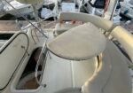 Cream-colored yacht deck seating area with an oval table, railings, and stairs to the cabin; moored in a marina.