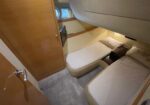 Compact boat cabin with two single beds along opposite walls, wood cabinetry, a small nightstand, and a porthole window above the left bed.