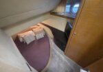 Small yacht cabin with a curved bed, purple cover, and striped pillows, wood cabinet nearby, and a round porthole window above.