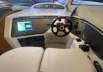 Luxury boat helm with wood steering wheel, navigation screen, and throttle levers in beige cabin.