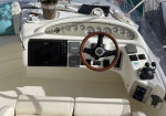 Yacht helm with wooden steering wheel, gauges, and navigation screens amid a white cockpit interior.