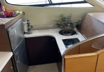 Boating galley with a small fridge, countertop, stove, and a potted plant by a curved window.