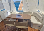Outdoor yacht deck seating area with a wooden table and cream cushions, overlooking blue water and sails foldable around.