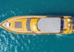 Top-down view of a yellow luxury yacht cruising on blue water.