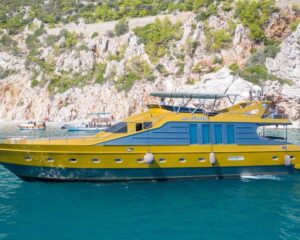 2007-custom-85-motor-yacht-power-10030822-20251205052641118-4 | Boat Universe Yellow and blue luxury motor yacht anchored near rocky cliffs with turquoise water and clear sky behind it.
