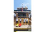 Six crew members in white shirts stand at the rear of a gold luxury yacht, with red and yellow kayaks on the deck.