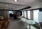Interior of a stylish yacht lounge with curved brown-and-cream walls, a white curved bar, and large windows with blinds along the right side.