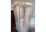 White curved shower cabin with full-body hydrojet panel and handheld shower head in a small bathroom.