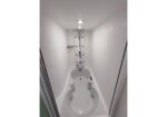 White narrow whirlpool tub with a vertical shower panel and multiple jets against white walls on a compact bath.