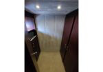 Narrow wooden closet with two tall doors, beige carpet, and an open left cabinet holding folded towels; ceiling lights above.