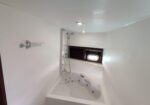 White bathroom with a built-in corner jacuzzi tub, wall-mounted shower panel, and a small porthole window.