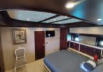 Luxurious yacht cabin with a large bed, built-in dark wood cabinets, a wall-mounted TV, and porthole windows on either side