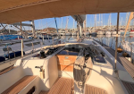 Sailing boat deck in a marina with rope lines coiled on a pedestal and wooden cockpit, view toward moored sailboats under a clear sky