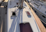 Top-down view of a white sailboat deck in a crowded marina, with a closed hatch, rigging, and neighboring boats on both sides in warm sunlight.