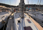 Sailboat deck in a marina, surrounded by other docked boats, rigging and masts against a clear sky.