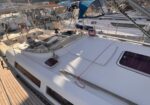 Sailboat deck at a marina with multiple moored sailboats, rigging, and a sunlit wooden deck.