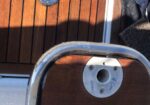 Close-up of a wooden boat deck with vertical teak planks, a circular metal fitting, and chrome trim at the edge of a step.