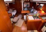 Cozy yacht saloon with wooden cabinetry, a central dining table, and L-shaped seating - includes a compact galley with sink on the right.