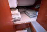 Wood-paneled boat cabin bunk with a mattress, folded blankets, and stacked cushions on the side