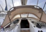 Sailboat cockpit with canopy open, coiled lines and winches, leading to a hatch into the cabin at a marina.