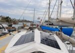 Sailboat in a marina with a solar-panel canopy over the cockpit and tall masts in the background