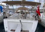 White sailboat at a marina with a ramp gangway leading to the stern and a Turkish flag flying from the stern area, other boats in the background.