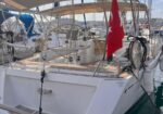 White sailboat docked in a marina with a Turkish flag at the stern and fenders along the side.