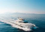 White luxury motor yacht cruising on calm blue sea with distant hazy mountains on the horizon.