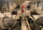 Engine room with two white industrial engines, black insulated hoses, and a red fire extinguisher at the back.
