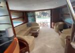 Luxurious yacht living area with cream leather sectional, curved wood accents, and a central oval coffee table; large windows and doors open to an outdoor seating area.